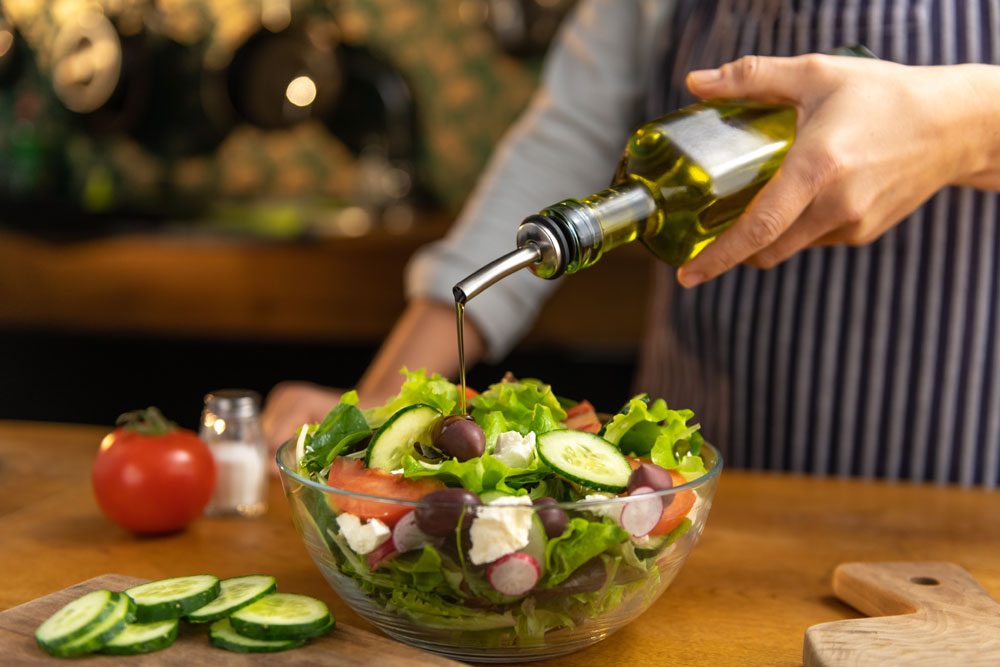Frau verwendet Olivenöl an Salat.