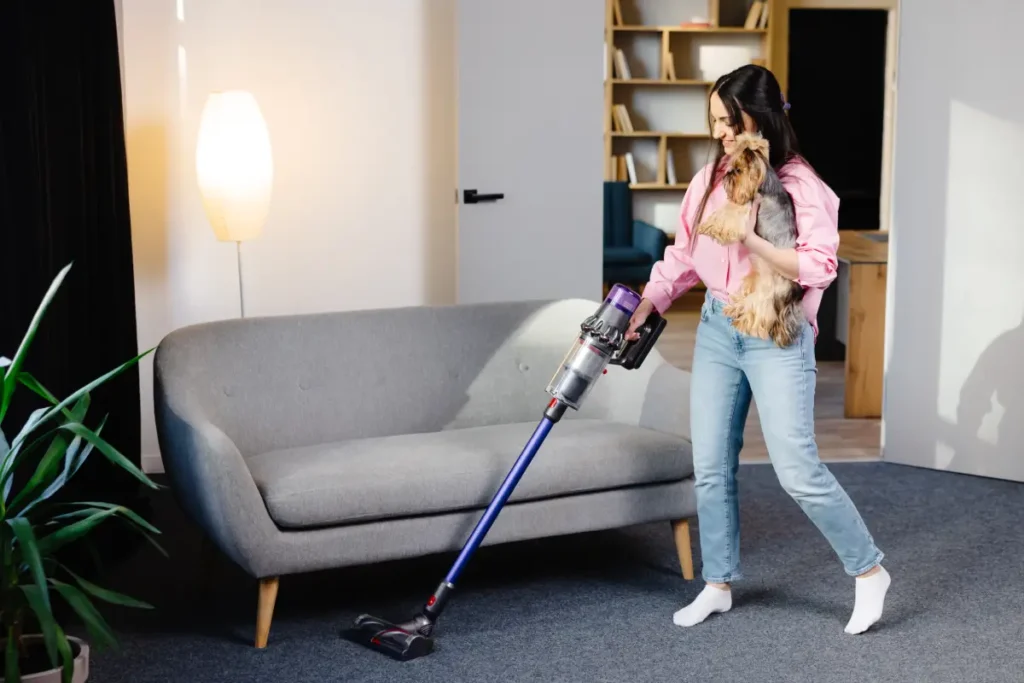 Frau mit Hund auf dem Arm saugt einen Teppich ab Gerüche aus dem Teppich entfernen - Die besten Hausmittel & Tipps für einen frischen Duft